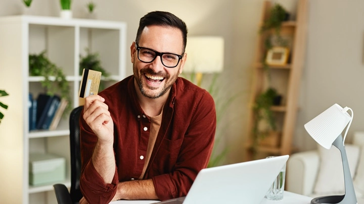 Ein Mann hält lächelnd seine Kreditkarte in der Hand